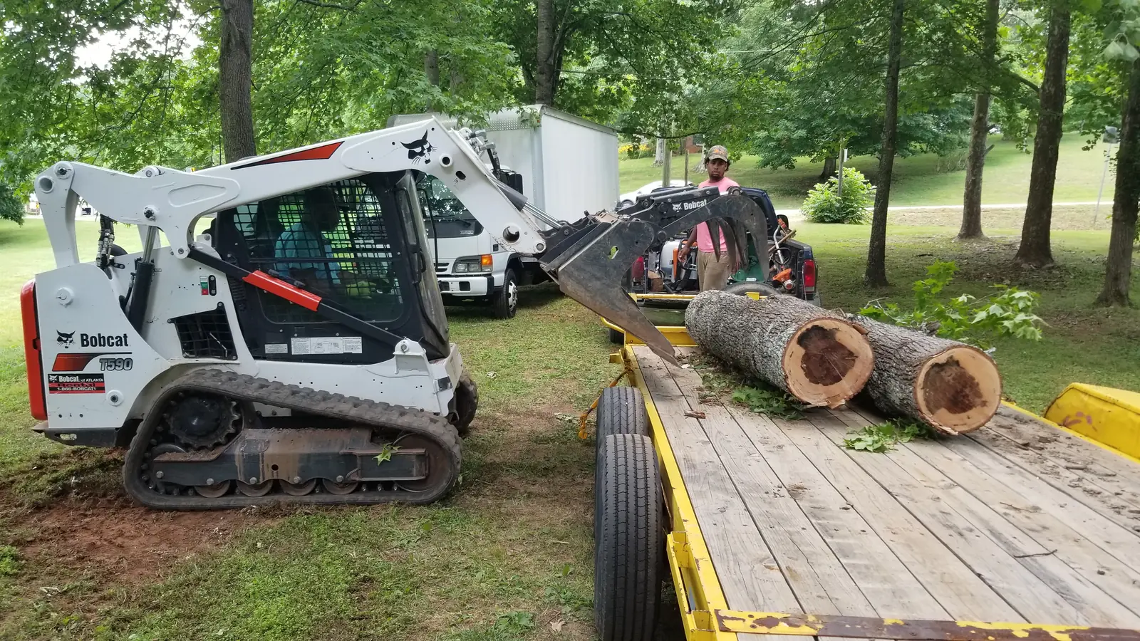 Cant Stop crew member loading cut logs onto a trailer next to the company's tracked Bobcat