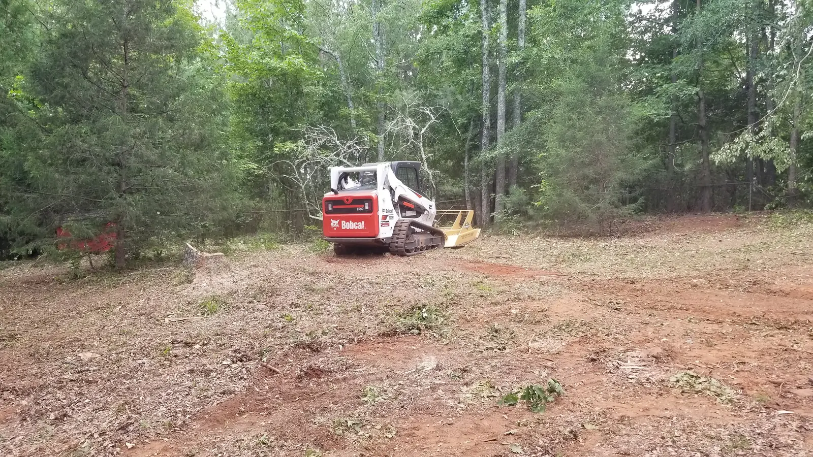 Cleared red-clay lot with the Bobcat working in the distance